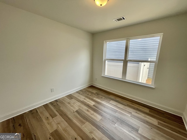 spare room with light wood-type flooring, visible vents, and baseboards