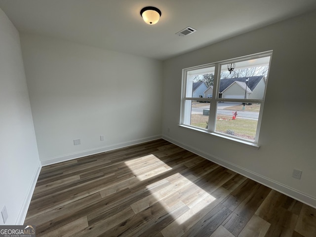 unfurnished room featuring dark wood finished floors, visible vents, and baseboards