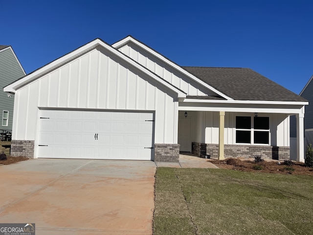 view of front of property with an attached garage, a shingled roof, concrete driveway, a front lawn, and board and batten siding