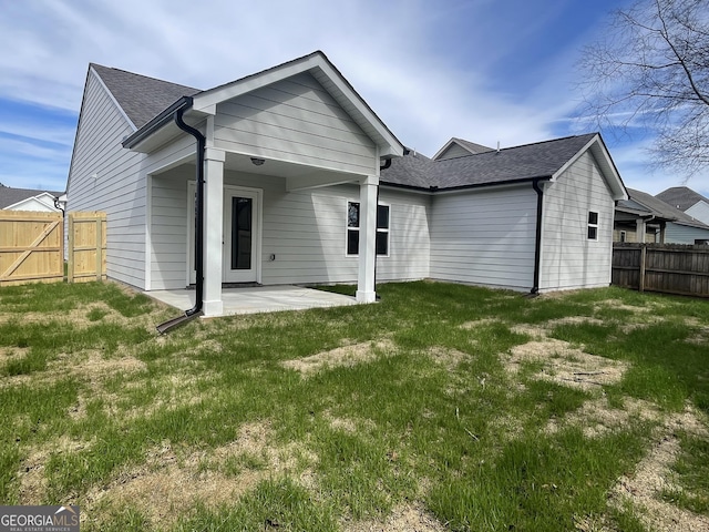 rear view of property with roof with shingles, a lawn, a patio, and fence