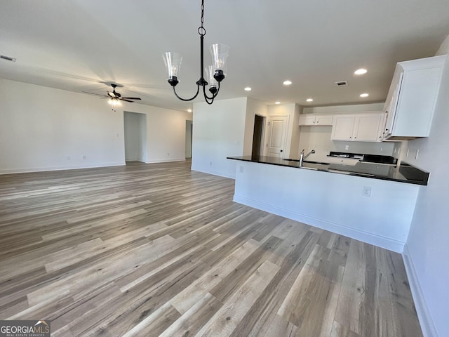 kitchen featuring ceiling fan with notable chandelier, white cabinetry, open floor plan, dark countertops, and pendant lighting