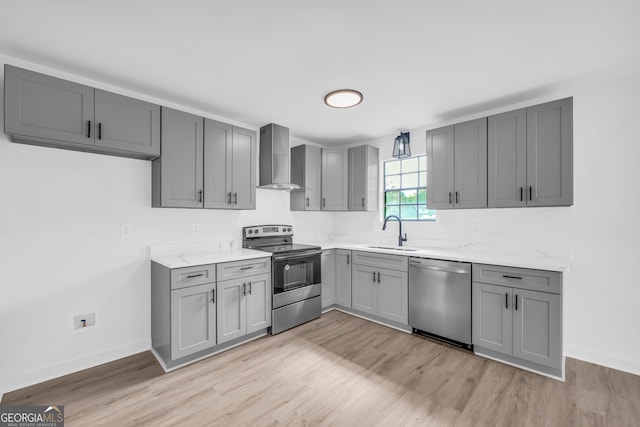 kitchen featuring appliances with stainless steel finishes, sink, wall chimney range hood, and light hardwood / wood-style flooring