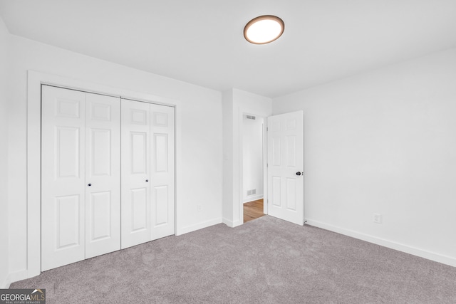 unfurnished bedroom with light colored carpet and a closet