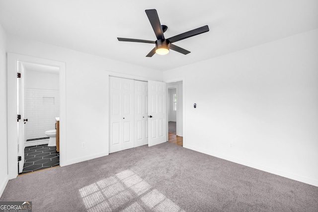 unfurnished bedroom featuring ceiling fan, a closet, dark colored carpet, and ensuite bathroom