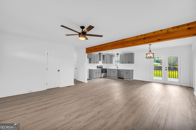 unfurnished living room with wood-type flooring, beam ceiling, ceiling fan, and sink