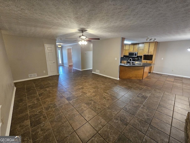 kitchen featuring dark countertops, stainless steel microwave, baseboards, and open floor plan