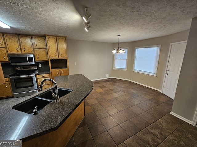 kitchen with a sink, stainless steel appliances, a textured ceiling, dark countertops, and brown cabinets