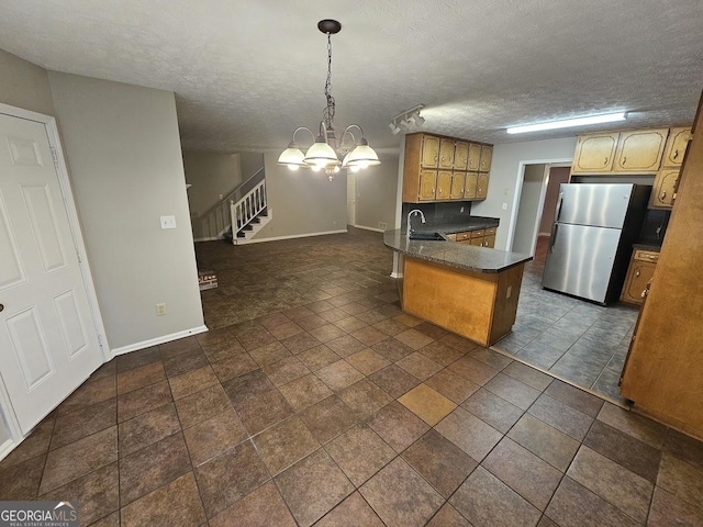 kitchen featuring a peninsula, freestanding refrigerator, pendant lighting, a textured ceiling, and dark countertops