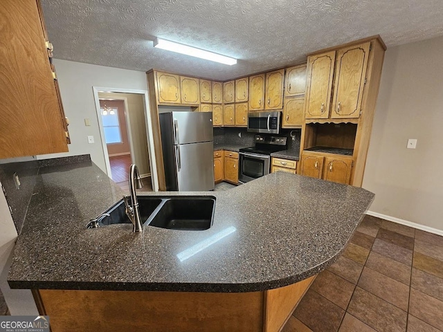 kitchen featuring baseboards, brown cabinets, appliances with stainless steel finishes, a peninsula, and a sink