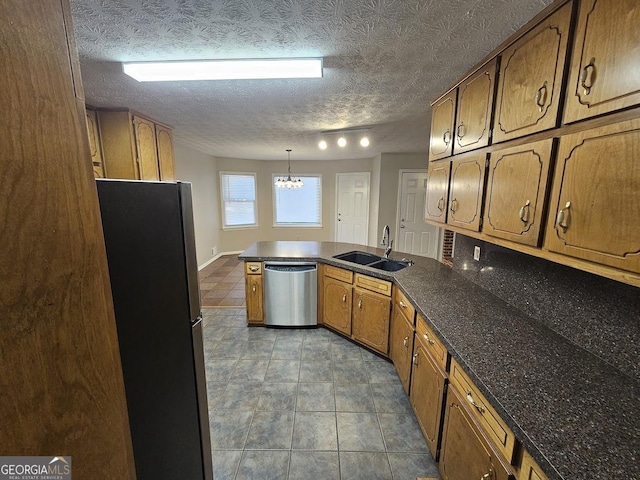 kitchen featuring brown cabinetry, a peninsula, a sink, stainless steel appliances, and dark countertops