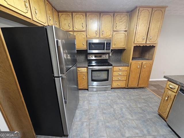 kitchen with light tile patterned floors, baseboards, stainless steel appliances, a textured ceiling, and dark countertops