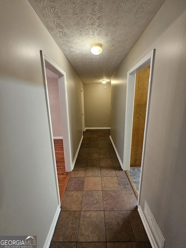 hallway with dark tile patterned flooring, baseboards, and a textured ceiling