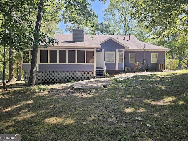 rear view of house featuring a yard, central AC unit, a chimney, and a sunroom