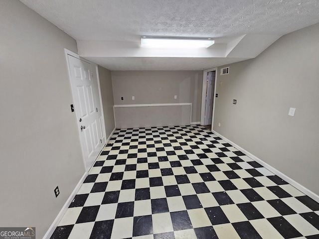 finished below grade area with tile patterned floors, visible vents, a textured ceiling, and baseboards