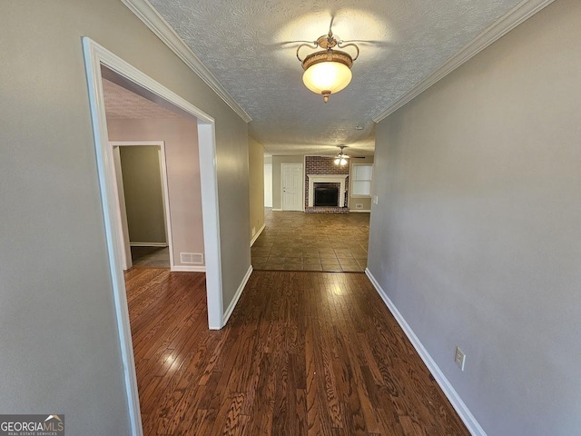 hall featuring baseboards, visible vents, dark wood-style flooring, ornamental molding, and a textured ceiling