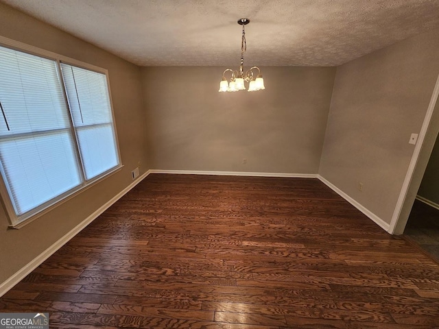 unfurnished dining area with baseboards, dark wood-type flooring, an inviting chandelier, and a textured ceiling