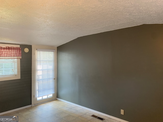 unfurnished room featuring vaulted ceiling and a textured ceiling