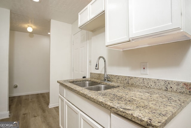 kitchen featuring white cabinets, light stone countertops, a textured ceiling, hardwood / wood-style flooring, and sink