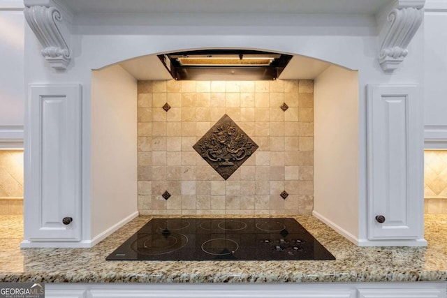 room details featuring black electric cooktop, white cabinets, light stone counters, and decorative backsplash