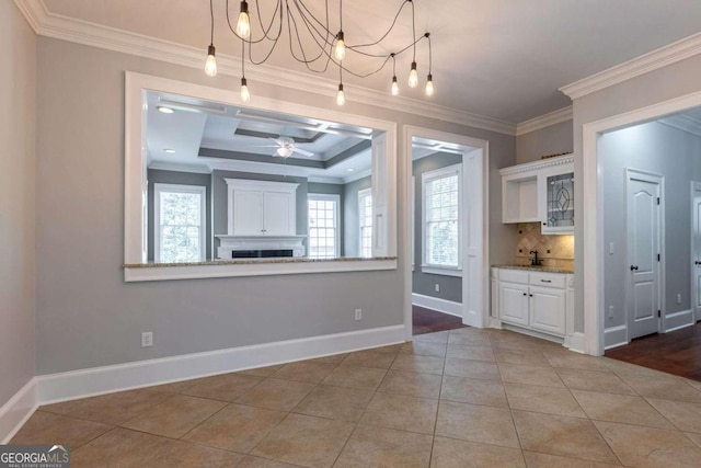 interior space with ceiling fan with notable chandelier, a tray ceiling, ornamental molding, and light tile patterned floors