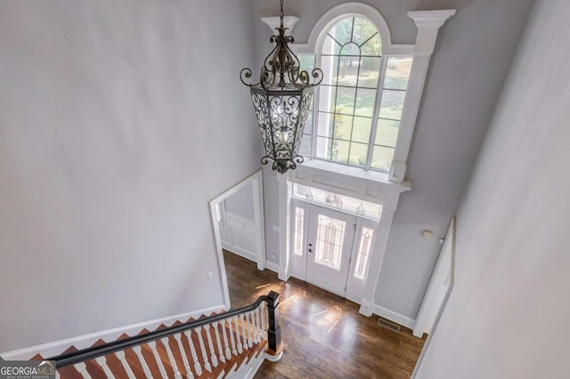 foyer entrance with an inviting chandelier, a towering ceiling, and dark hardwood / wood-style flooring