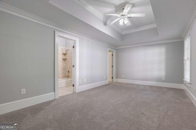 unfurnished bedroom featuring crown molding, a tray ceiling, ceiling fan, ensuite bathroom, and light colored carpet