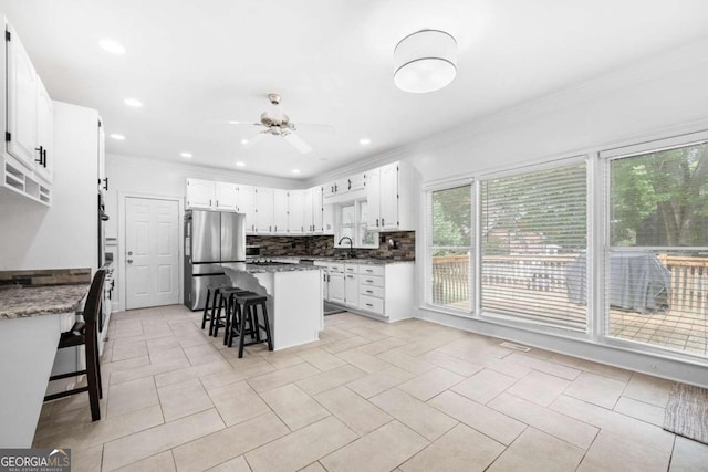 kitchen with a kitchen island, white cabinetry, dark stone counters, stainless steel refrigerator, and a breakfast bar area