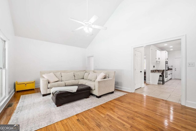 living room with ceiling fan, high vaulted ceiling, and light wood-type flooring