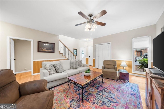 living room featuring light wood-type flooring, wooden walls, and ceiling fan