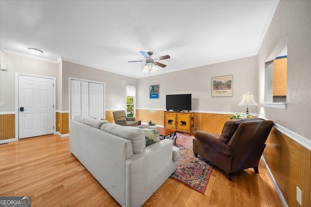 living room featuring light hardwood / wood-style flooring, wooden walls, ceiling fan, and crown molding