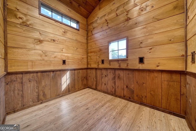 spare room featuring wooden walls, light wood-type flooring, and lofted ceiling