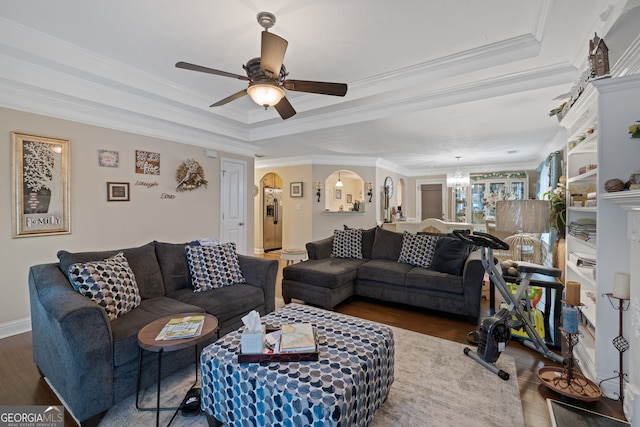 living room with ceiling fan with notable chandelier, a tray ceiling, ornamental molding, and dark hardwood / wood-style flooring