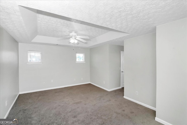 unfurnished room with a textured ceiling, a raised ceiling, ceiling fan, and plenty of natural light