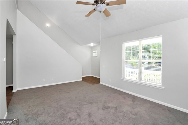 empty room with lofted ceiling, dark carpet, ceiling fan, and a wealth of natural light