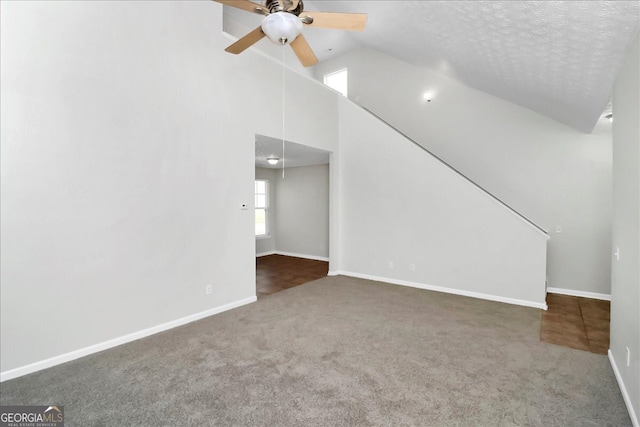 unfurnished living room featuring a textured ceiling, lofted ceiling, dark colored carpet, and ceiling fan