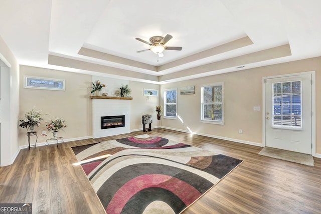 living room with ceiling fan, a tray ceiling, and dark hardwood / wood-style flooring