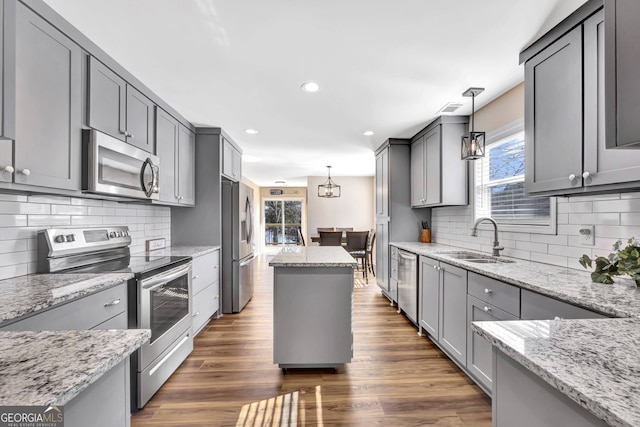 kitchen with appliances with stainless steel finishes, gray cabinetry, dark hardwood / wood-style flooring, pendant lighting, and sink