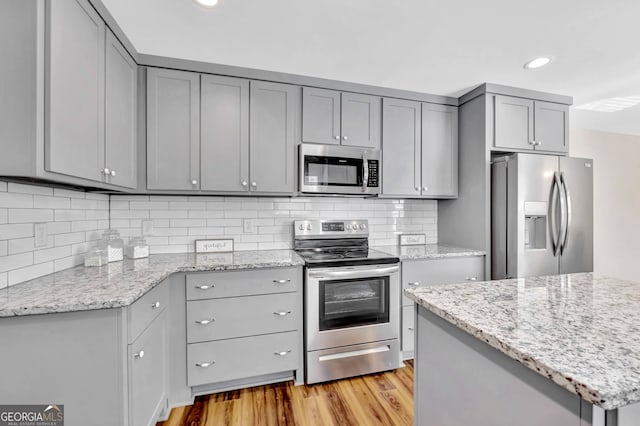 kitchen with light hardwood / wood-style flooring, stainless steel appliances, light stone counters, and gray cabinets