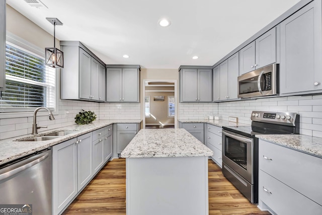 kitchen with hanging light fixtures, backsplash, stainless steel appliances, a center island, and light hardwood / wood-style flooring