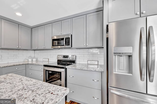 kitchen featuring light stone countertops, gray cabinetry, appliances with stainless steel finishes, and tasteful backsplash