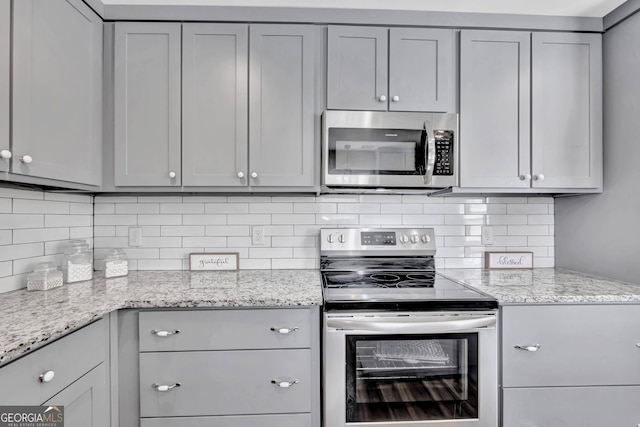 kitchen featuring gray cabinets, stainless steel appliances, decorative backsplash, and light stone countertops