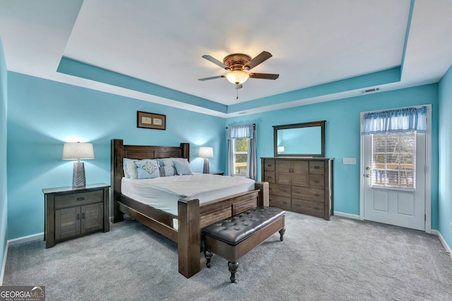 bedroom featuring light carpet, a tray ceiling, and ceiling fan