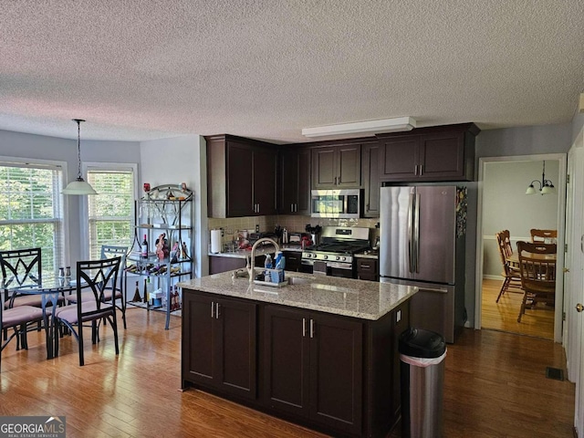 kitchen with dark brown cabinets, stainless steel appliances, light stone counters, and hanging light fixtures