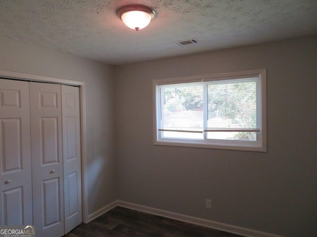 unfurnished bedroom with a textured ceiling, a closet, and dark hardwood / wood-style floors