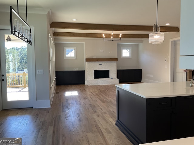 kitchen with beam ceiling, an inviting chandelier, a brick fireplace, decorative light fixtures, and hardwood / wood-style flooring