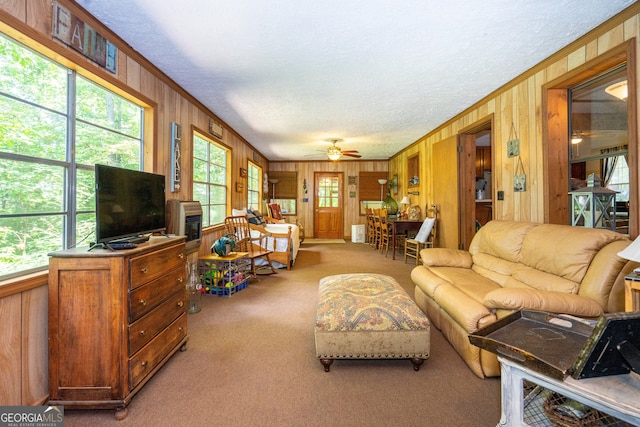 carpeted living room featuring ornamental molding, wooden walls, and ceiling fan