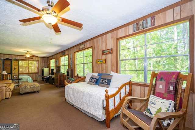 carpeted bedroom with wood walls, ceiling fan, and a textured ceiling