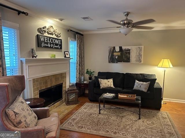 living room with ceiling fan, a fireplace, ornamental molding, and hardwood / wood-style flooring