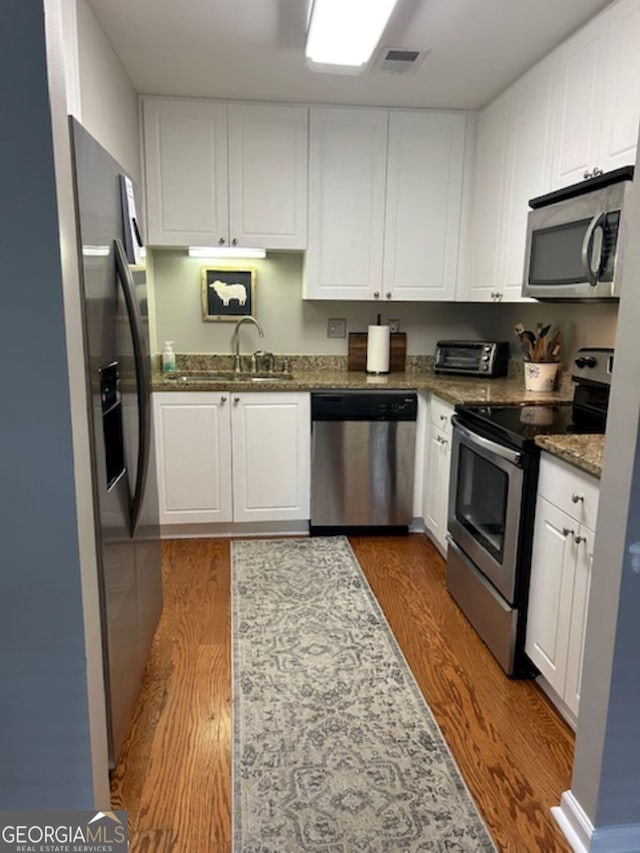 kitchen featuring stainless steel appliances, dark wood-type flooring, sink, dark stone countertops, and white cabinetry