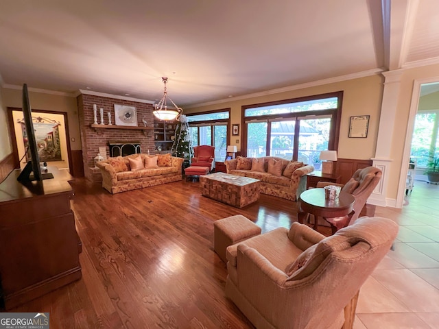 living room with decorative columns, a brick fireplace, plenty of natural light, and crown molding